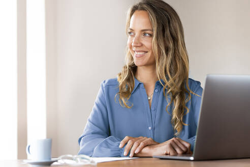 Lächelnde weibliche Fachkraft, die am Schreibtisch im Heimbüro träumt - SBOF03415