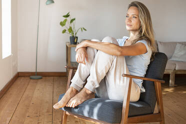 Beautiful woman contemplating while sitting on armchair at home - SBOF03439