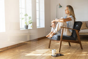 Woman day dreaming while sitting on chair at home - SBOF03440
