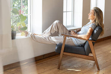 Frau mit Kaffeetasse entspannt sich auf einem Stuhl zu Hause - SBOF03459