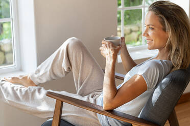 Happy woman looking away while having coffee at home - SBOF03462