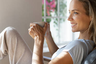 Lächelnde Frau hält Kaffeetasse zu Hause - SBOF03463