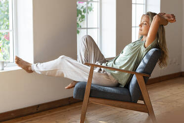 Woman with eyes closed resting on armchair at home - SBOF03465