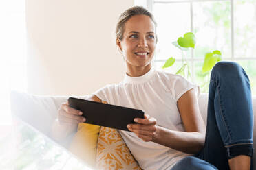 Smiling woman day dreaming while holding digital tablet on sofa - SBOF03509