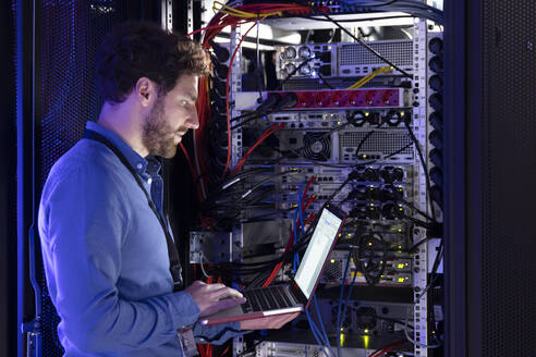 Männlicher IT-Spezialist arbeitet an einem Laptop im Serverraum - FKF04118