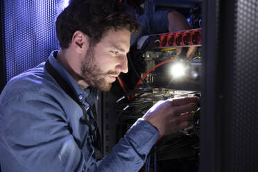 Männlicher IT-Ingenieur hält eine Taschenlampe, während er an einem Server-Rack im Rechenzentrum arbeitet - FKF04123
