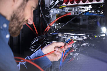 Männlicher IT-Spezialist bei der Installation von Patchkabel in einem Serverschrank im Rechenzentrum - FKF04132