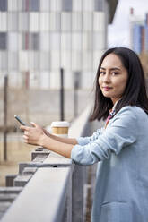 Young businesswoman with mobile phone leaning on railing - VEGF04124