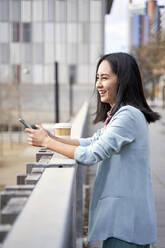 Businesswoman smiling and looking away while leaning on railing - VEGF04125