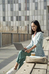 Junge Geschäftsfrau, die einen Laptop benutzt und auf einer Bank sitzt - VEGF04132