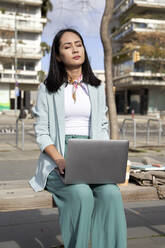 Junge Geschäftsfrau mit geschlossenen Augen sitzt mit Laptop auf einer Bank - VEGF04133