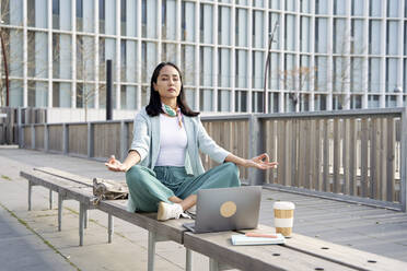 Businesswoman with eyes closed meditating on bench at footpath - VEGF04138