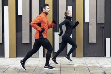 Entschlossene männliche und weibliche Freunde joggen auf dem Fußweg an der Mauer - JSRF01459
