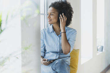 Woman adjusting headphones while sitting with digital tablet at home - SBOF03524
