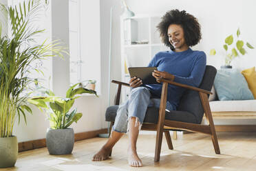 Young woman using digital tablet while sitting on armchair at home - SBOF03539