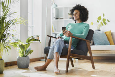 Smiling woman using mobile phone while sitting at home - SBOF03540