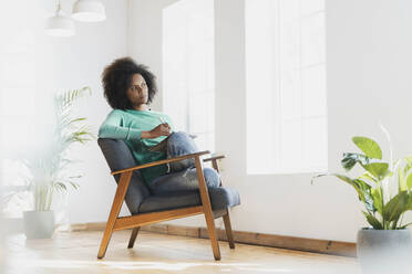 Frau, die mit einem Buch auf einem Sessel zu Hause sitzt und träumt - SBOF03547