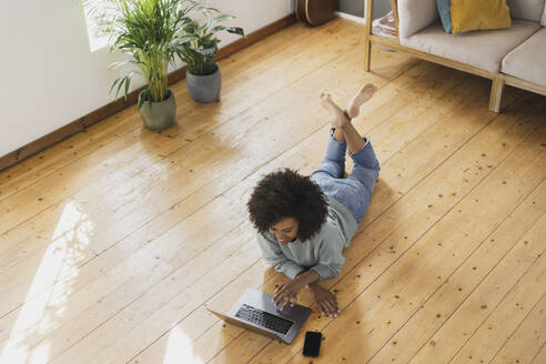 Frau benutzt Laptop und ruht sich zu Hause auf dem Boden aus - SBOF03554
