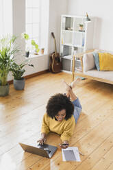 Smiling woman using mobile phone while lying on floor by laptop at home - SBOF03555