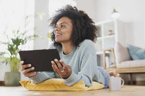 Junge Frau mit digitalem Tablet, das zu Hause auf dem Boden liegt - SBOF03558