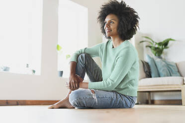 Young thoughtful woman looking away while sitting on floor at home - SBOF03563