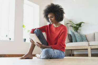 Young woman reading book while sitting in living room - SBOF03564