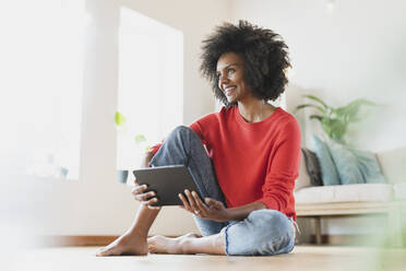 Lächelnde Frau hält digitales Tablet, während sie zu Hause auf dem Boden sitzt - SBOF03566