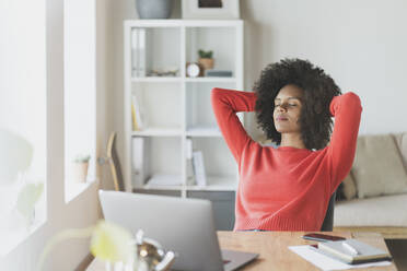 Young woman with hands behind head by laptop at home - SBOF03575