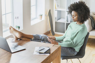 Woman using mobile phone while sitting on chair at home - SBOF03576