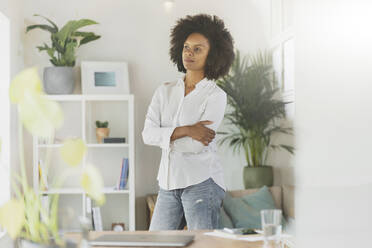 Thoughtful woman standing with arms crossed in living room - SBOF03587