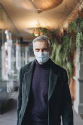 Man in jacket and protective face mask at hotel corridor - DGOF02017