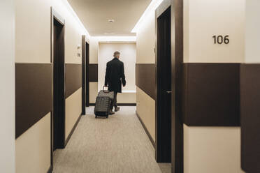Businessman walking with briefcase and luggage at hotel corridor - DGOF02039