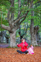 Mother playing with daughter while sitting on fallen leaves at Gorbea Natural Park - DSGF02398