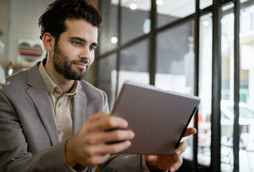 Mid adult businessman working on digital tablet in coffee shop - RCPF00883