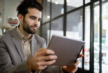 Mittlerer erwachsener Geschäftsmann, der in einem Café an einem digitalen Tablet arbeitet - RCPF00883