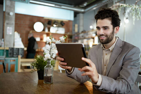 Lächelnder Geschäftsmann bei einem Videogespräch über eine digitale Tafel in einem beleuchteten Café - RCPF00884