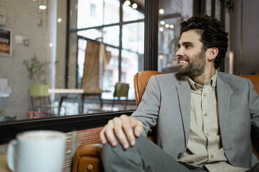 Happy female professional looking away while sitting on armchair in cafe - RCPF00885