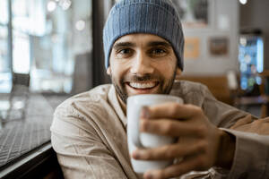 Glücklicher erwachsener Mann mit Kaffeetasse in einem Cafe - RCPF00895