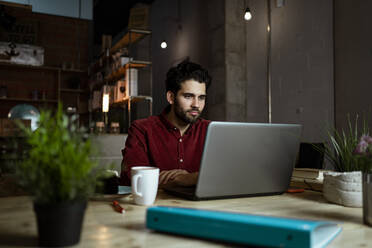 Mittlerer erwachsener männlicher Freiberufler mit Kaffeetasse, der in einem Café am Laptop arbeitet - RCPF00907