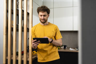 Handsome man using digital tablet while standing in domestic kitchen - VPIF03855