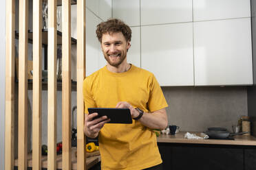 Smiling mid adult man holding digital tablet in domestic kitchen - VPIF03856