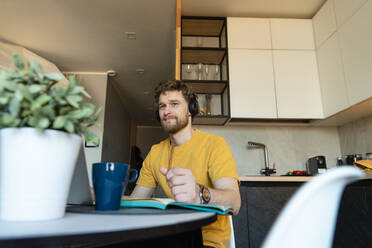 Male professional with pen listening music while looking away in domestic kitchen - VPIF03863