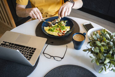 Geschäftsmann isst Omelett und Gemüse, während er mit seinem Laptop an einem Tisch im Haus sitzt - VPIF03869