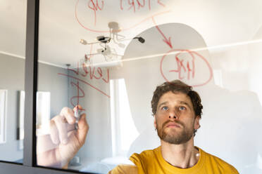 Male freelancer writing on glass while working at home - VPIF03870