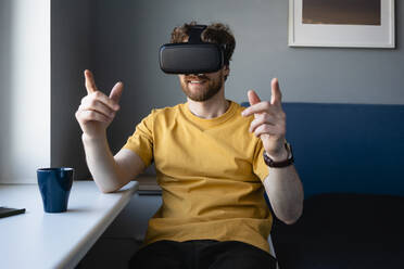 Mittlerer erwachsener Mann, der einen Virtual-Reality-Simulator benutzt, während er zu Hause im Wohnzimmer sitzt - VPIF03873