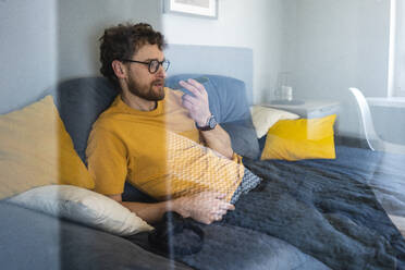 Man talking on mobile phone while sitting on sofa at home - VPIF03883