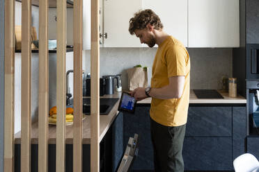 Mittlerer Erwachsener, der in der Küche einen Ofen mit einem digitalen Tablet bedient - VPIF03885