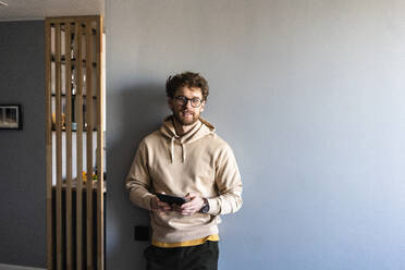 Mann mit Brille hält digitales Tablet und lehnt sich zu Hause an die Wand - VPIF03897