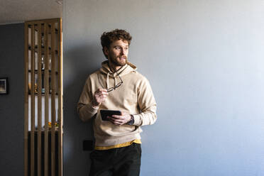 Mann mit digitalem Tablet, der wegschaut, während er zu Hause steht - VPIF03898