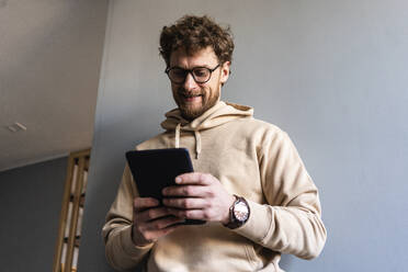 Lächelnder Mann mit Brille, der zu Hause ein digitales Tablet benutzt - VPIF03900